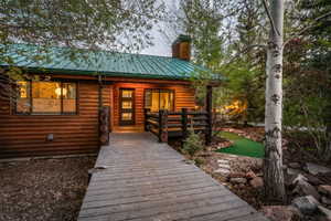 Log cabin exterior featuring a green metal roof, a wooden front deck, and a modern dark-framed entry door