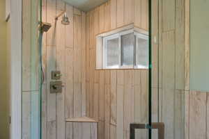 Walk-in shower featuring glass enclosure, wood-look tile, rainfall showerhead, handheld shower fixture, and an integrated corner bench