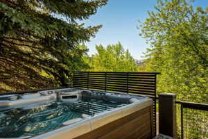 Outdoor hot tub with wood-finish siding, positioned on a deck with cable railing and slatted privacy screen