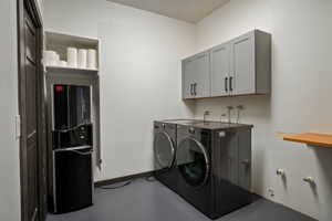 Laundry area featuring overhead gray cabinetry, integrated washer and dryer units, a built-in shelving unit, and a wall-mounted wooden shelf