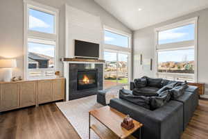Living area featuring vaulted ceilings, wood-finish flooring, and a fireplace with a stone surround and wood mantel