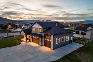 Modern two-story residence with dark siding, stone accents, and a prominent concrete driveway