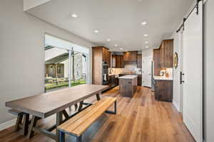 Open-concept kitchen and dining area featuring rich wood cabinetry, stainless steel appliances, a center island with a white countertop, and wood-finish flooring