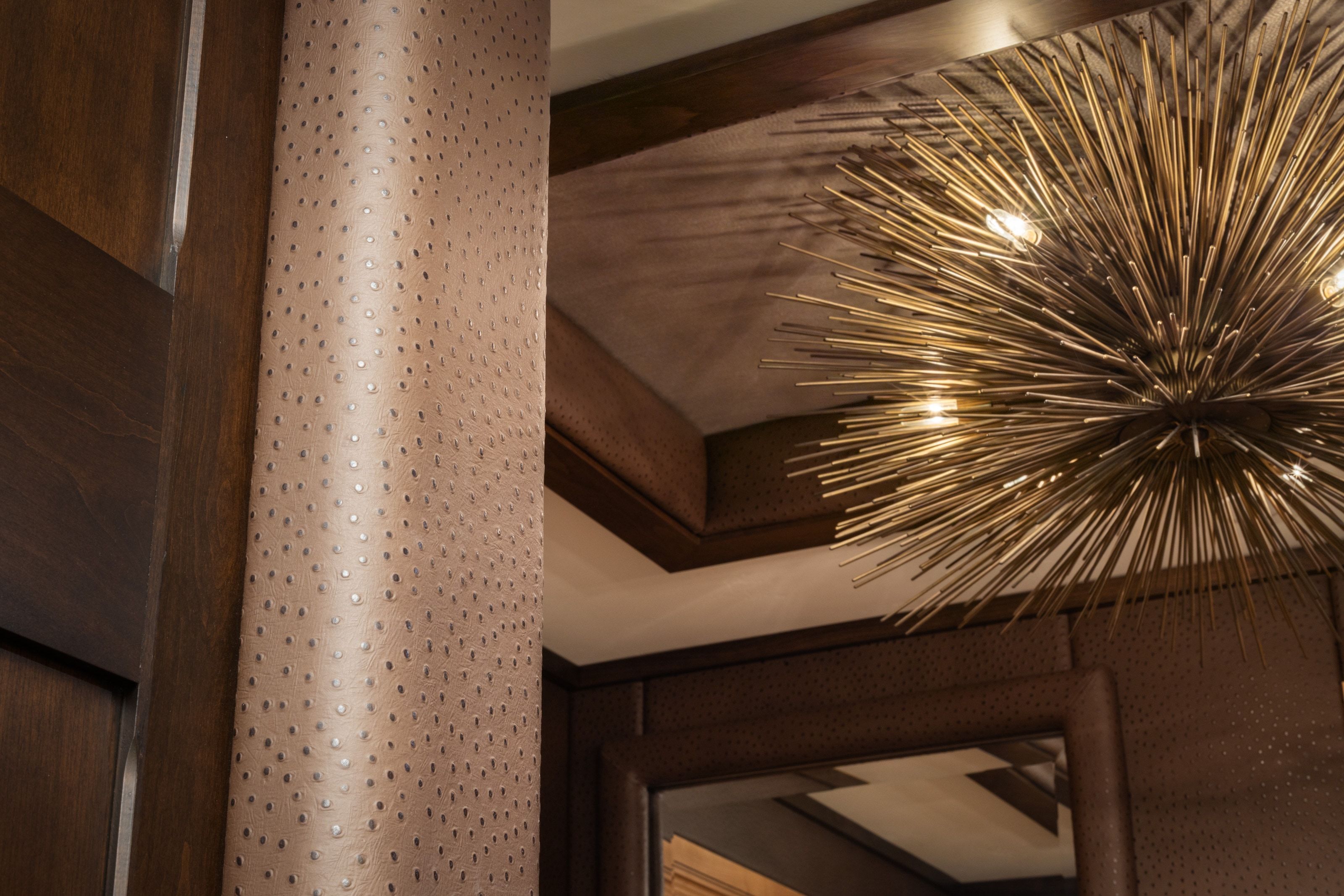 Decorative sputnik-style chandelier illuminating a ceiling with detailed trim work, alongside a column wrapped in a textured, perforated material, complemented by dark wood paneling