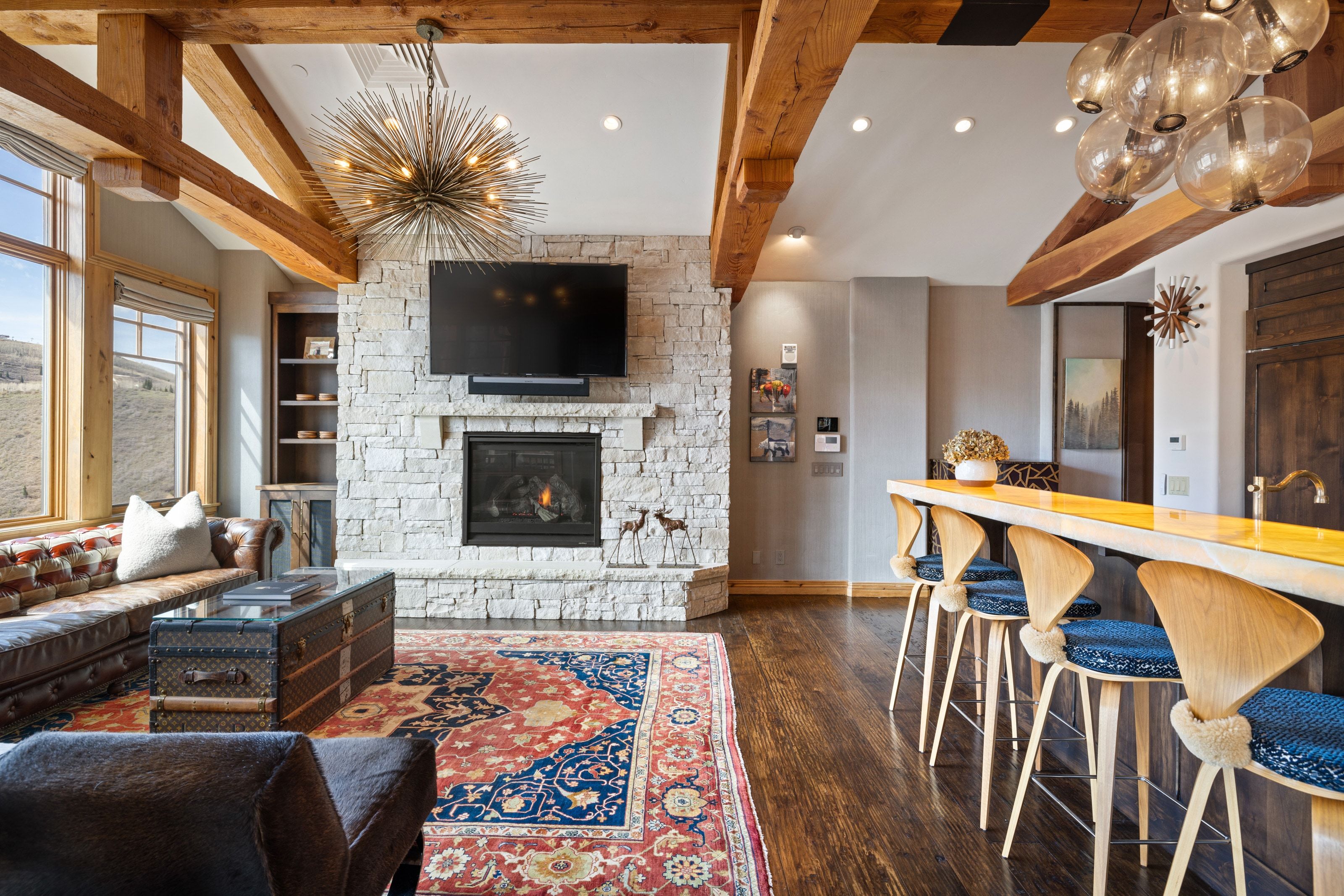 Living space featuring a stone-clad fireplace, exposed wood ceiling beams, and wood-finish flooring