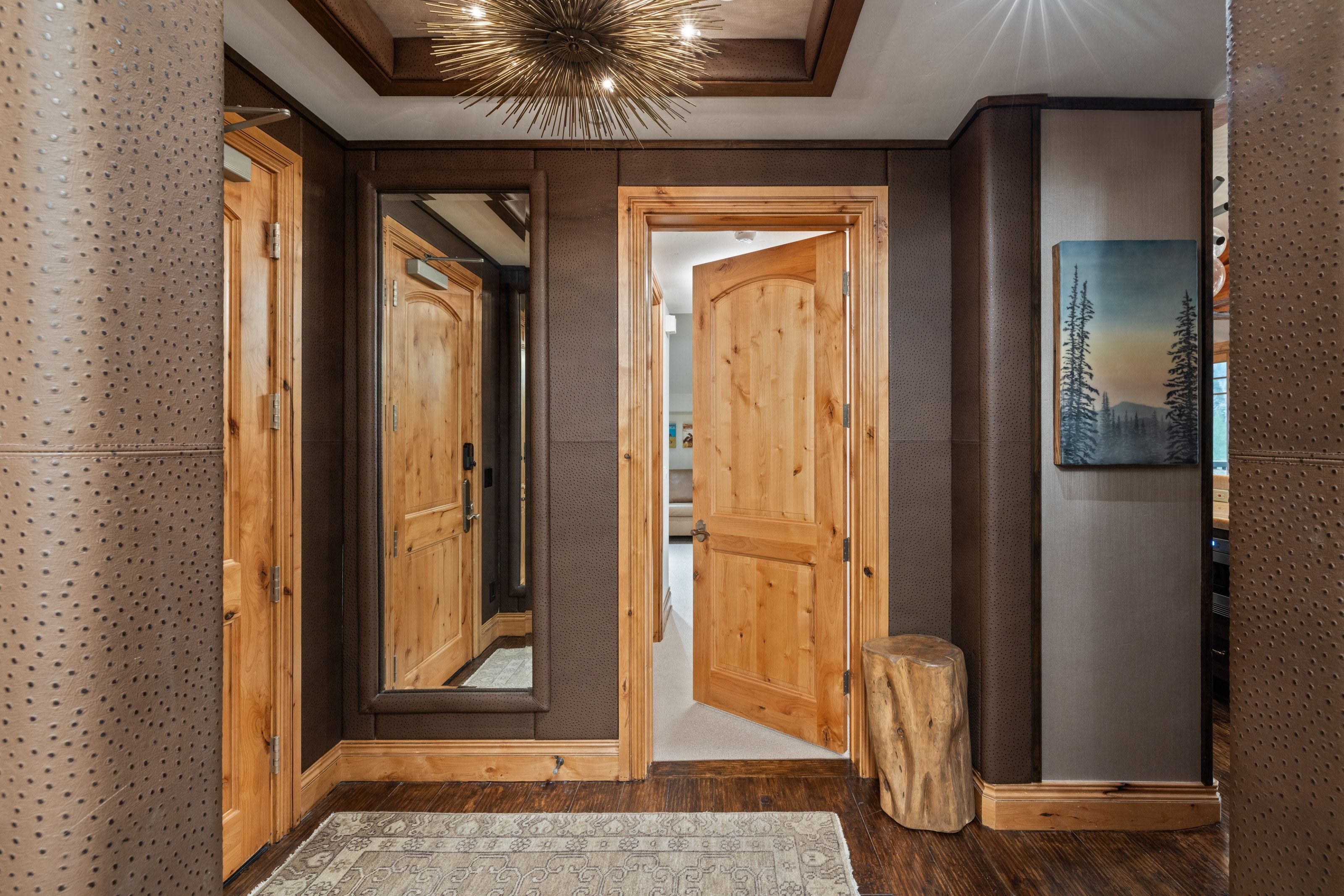 Entryway featuring natural wood doors, wood-finish flooring, a full-length mirrored accent, textured wall panels, and a distinctive overhead light fixture