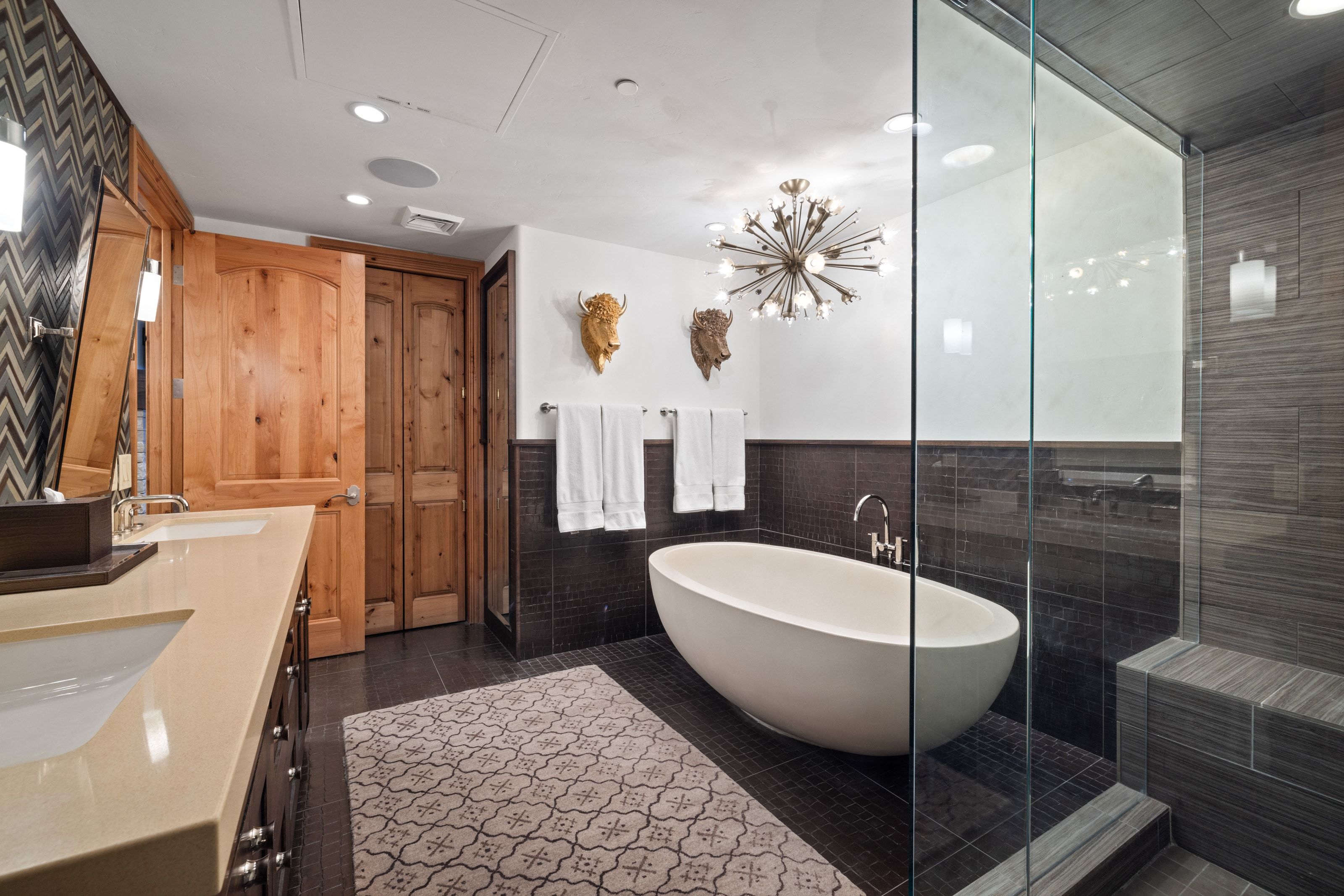 Contemporary bathroom featuring a freestanding soaking tub, glass-enclosed shower with tiled bench, dual vanity with undermount sinks and light-toned countertops, and wood-panel doors