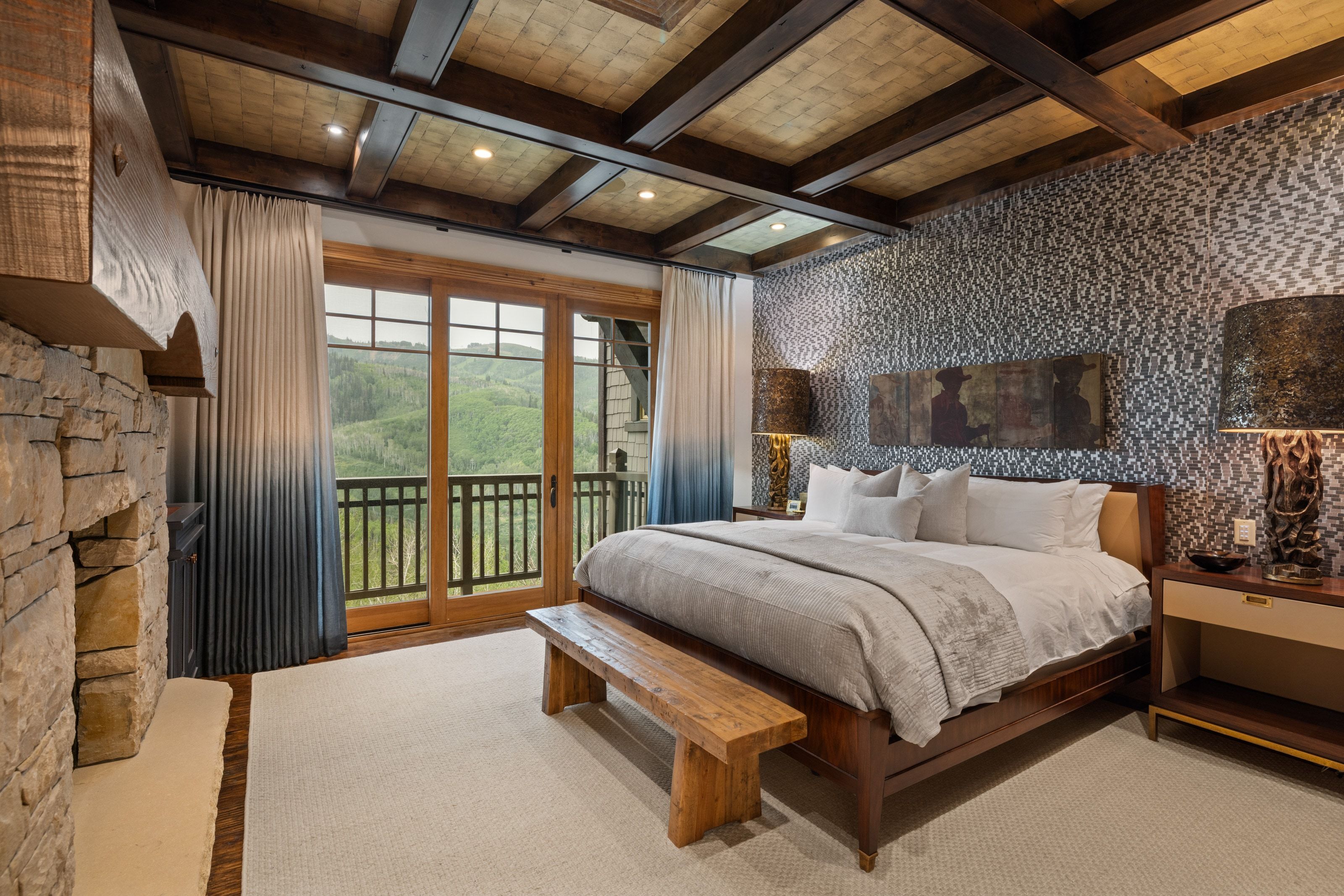 Room featuring a stone-faced fireplace with a wood mantel, wood-beam ceiling, and a full wall of glass doors opening to a balcony with mountain scenery