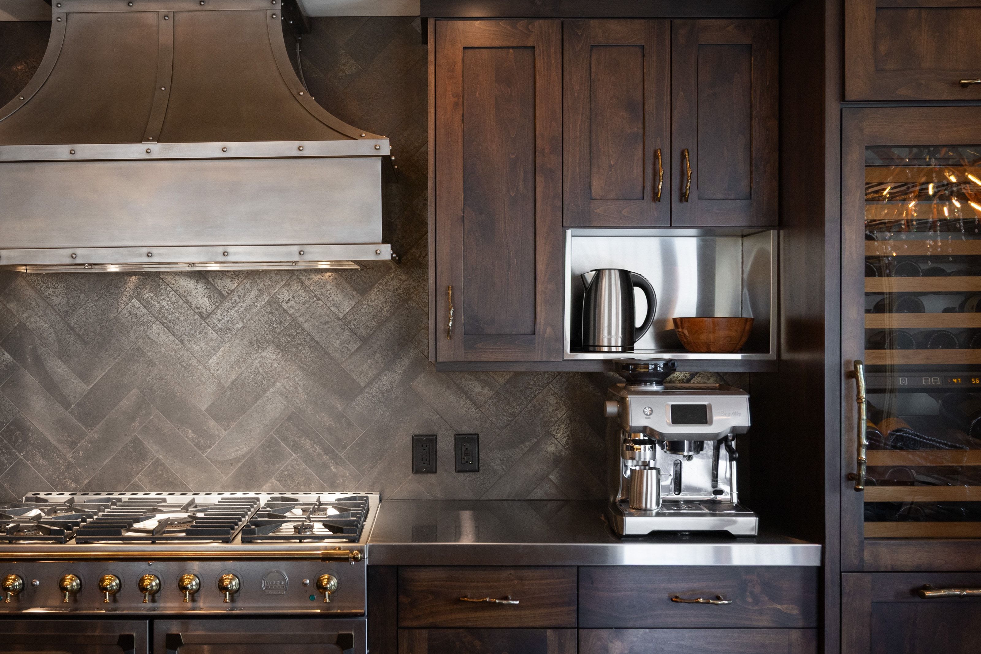 Gourmet kitchen featuring a professional-grade range, custom metal range hood, dark wood cabinetry, a built-in wine refrigerator, and stainless steel countertops