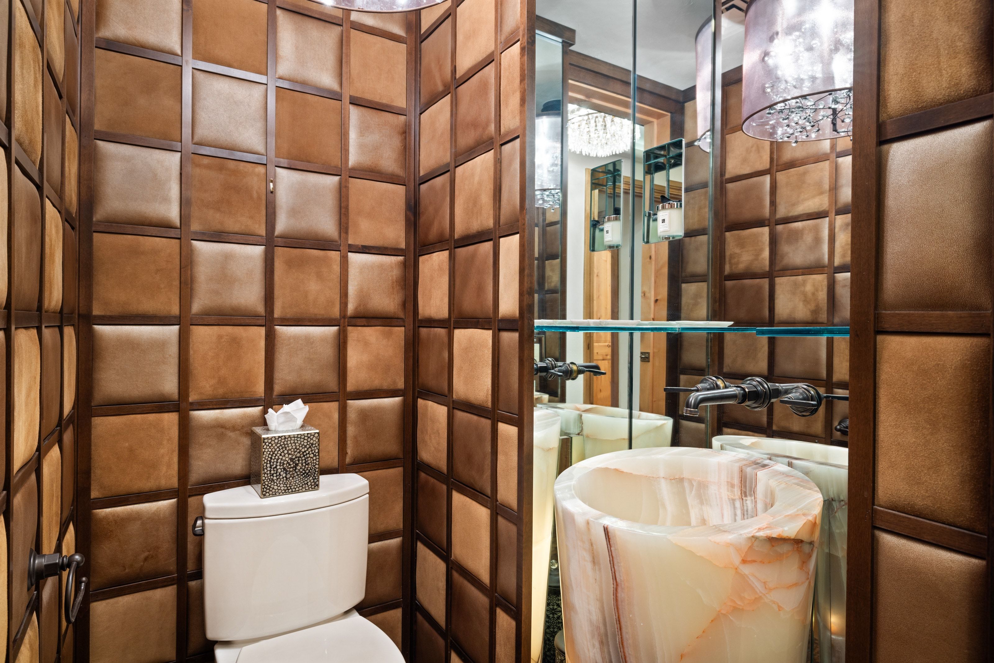 Powder room featuring padded wall panels with wood framing, a pedestal sink crafted from a light-toned, veined stone, and a wall-mounted faucet with an industrial design