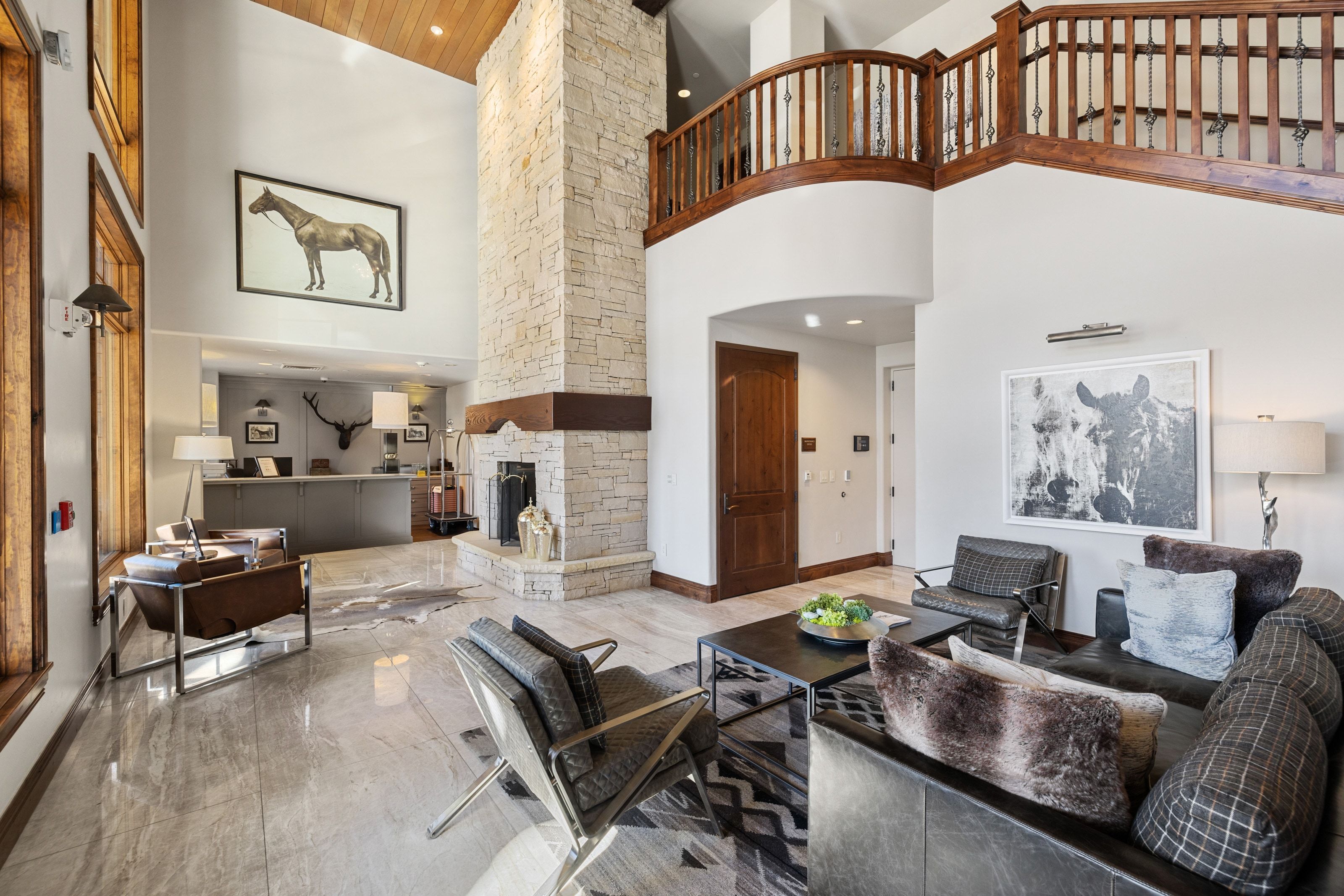 Spacious living area featuring a two-story stone fireplace, high vaulted ceilings with wood paneling, and polished stone flooring