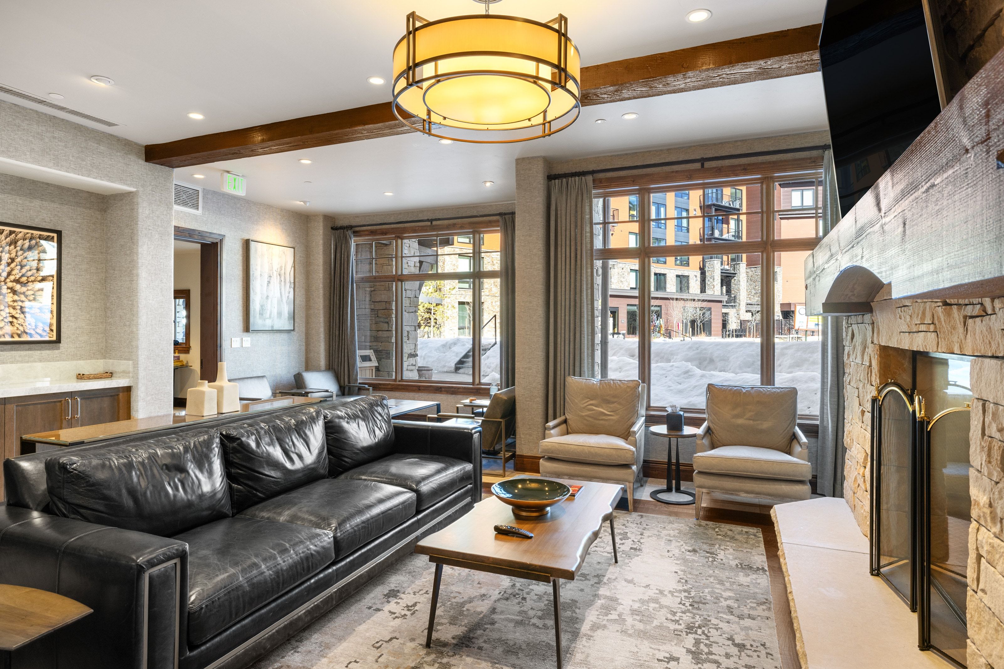 Spacious living area featuring a stone fireplace, large windows with exterior views, exposed wood beam accents, a built-in wet bar, and recessed lighting