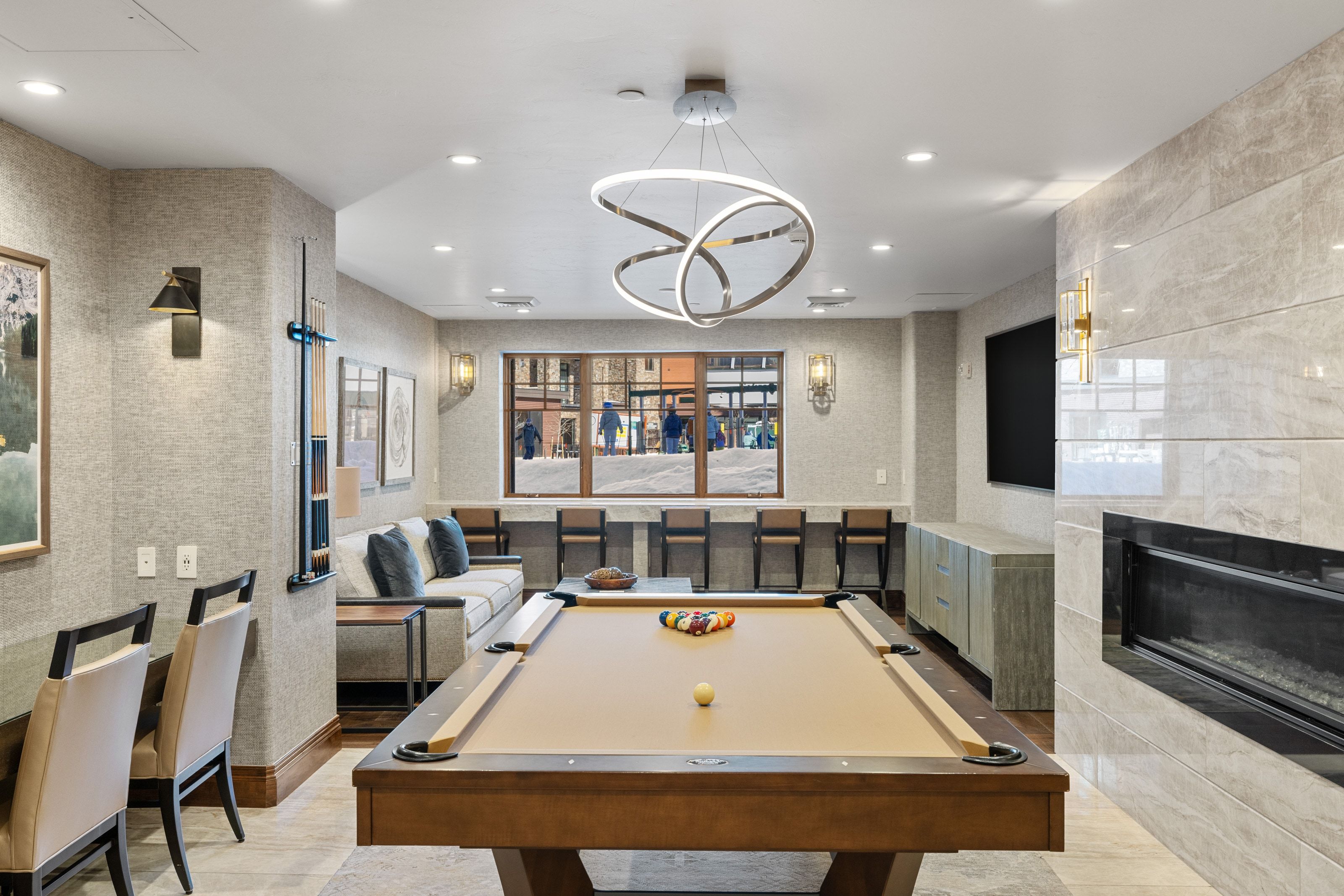 Recreational room featuring a billiards table, a contemporary linear fireplace with a stone-finish surround, a window-front bar area, and a built-in media console