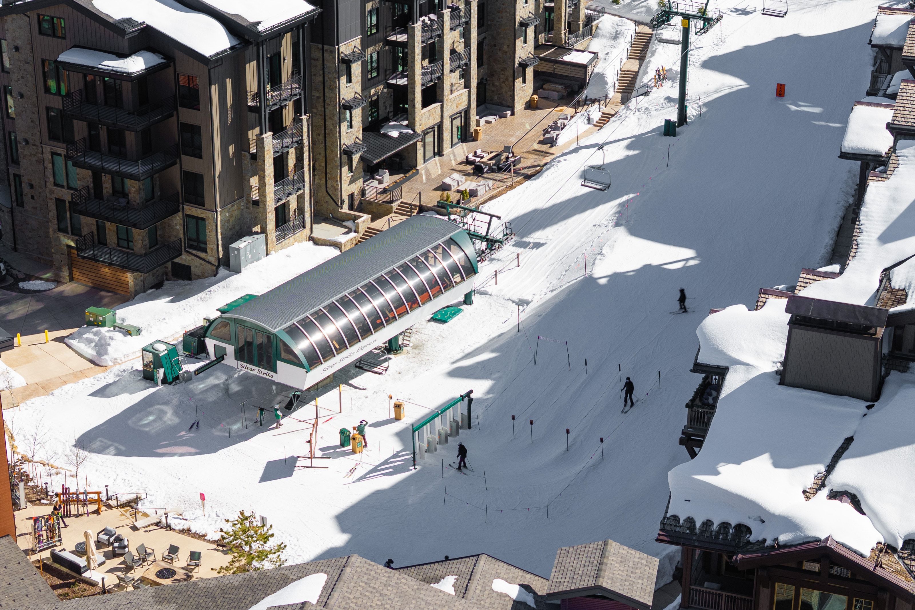 Ski resort setting featuring a ski lift base station, adjacent snow-covered slopes, and multi-story buildings with balconies