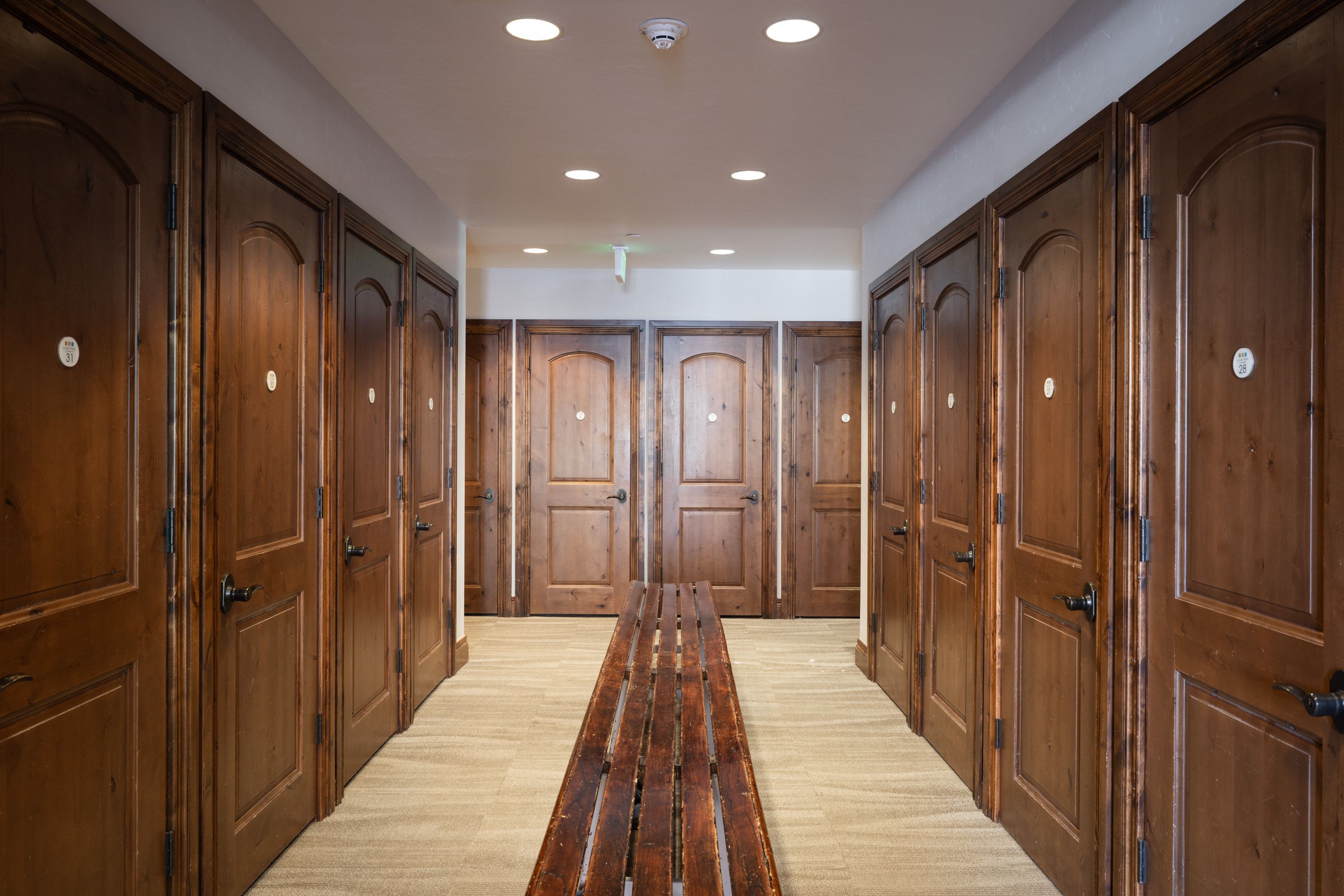 Hallway featuring multiple wood-finish doors with arched paneling and dark hardware