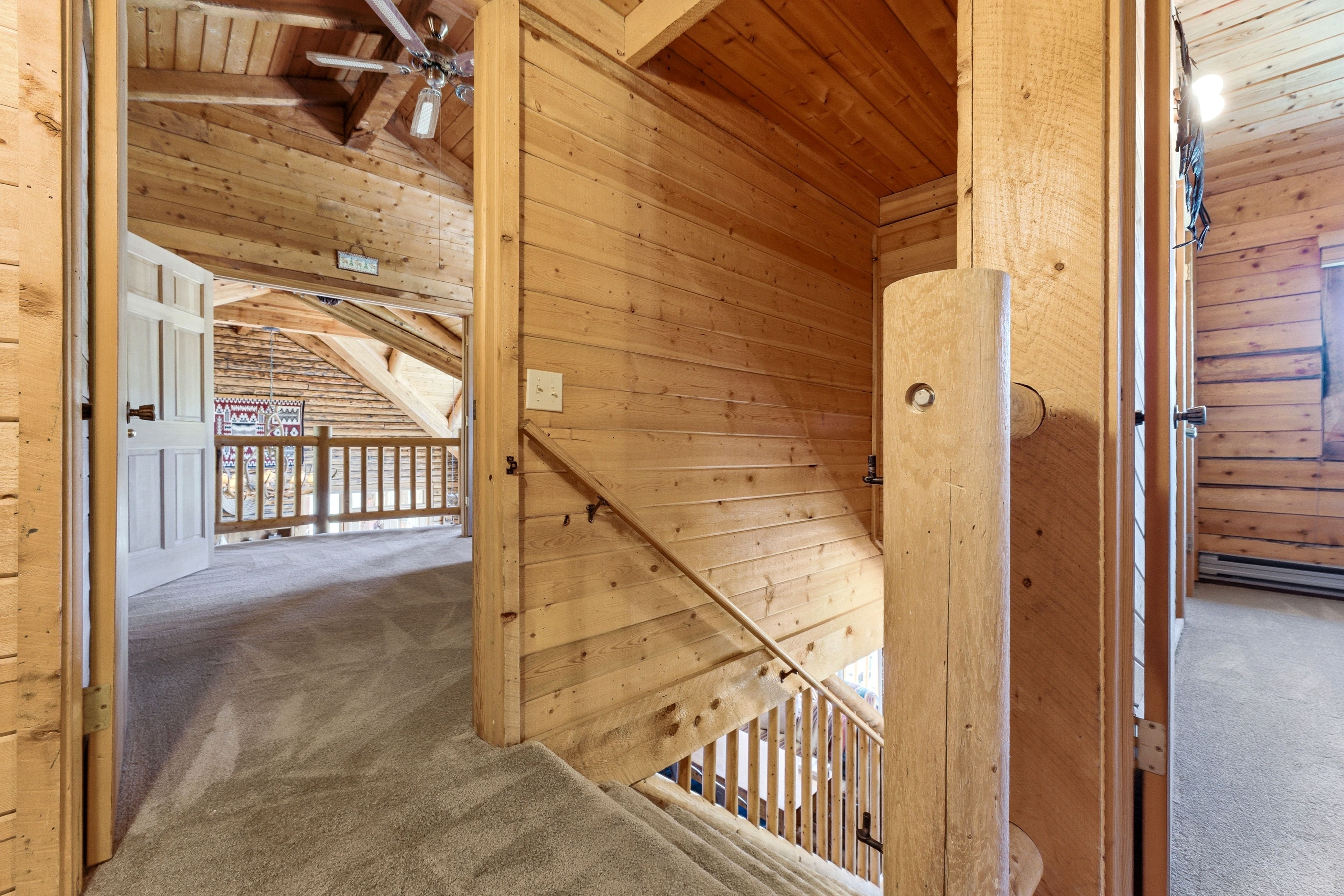 Expansive wood-paneled interior featuring a carpeted landing, staircase with wood railings, and a vaulted ceiling with a built-in ceiling fan