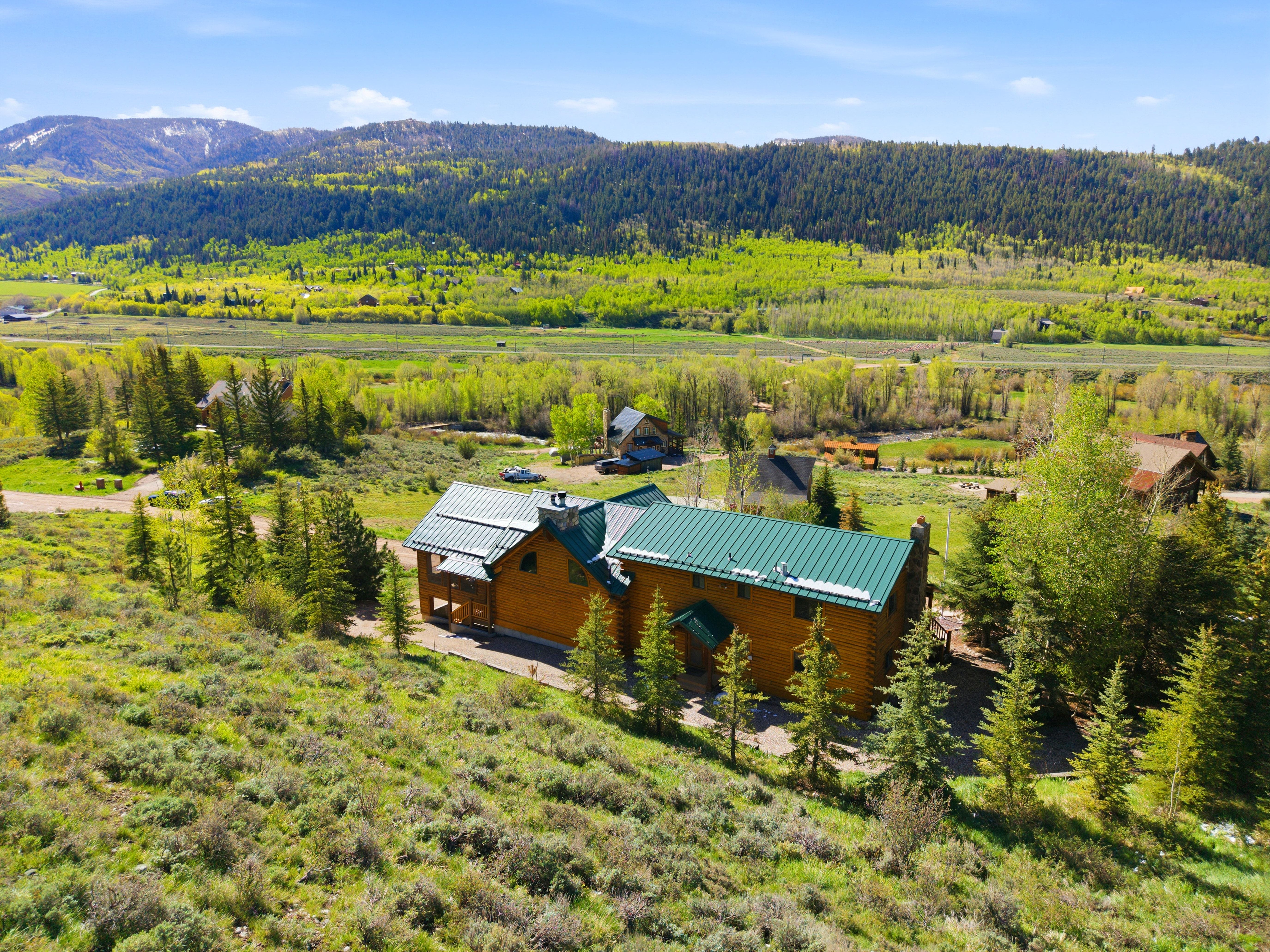 Log-style residence featuring a green metal roof, multiple chimneys, and a covered porch
