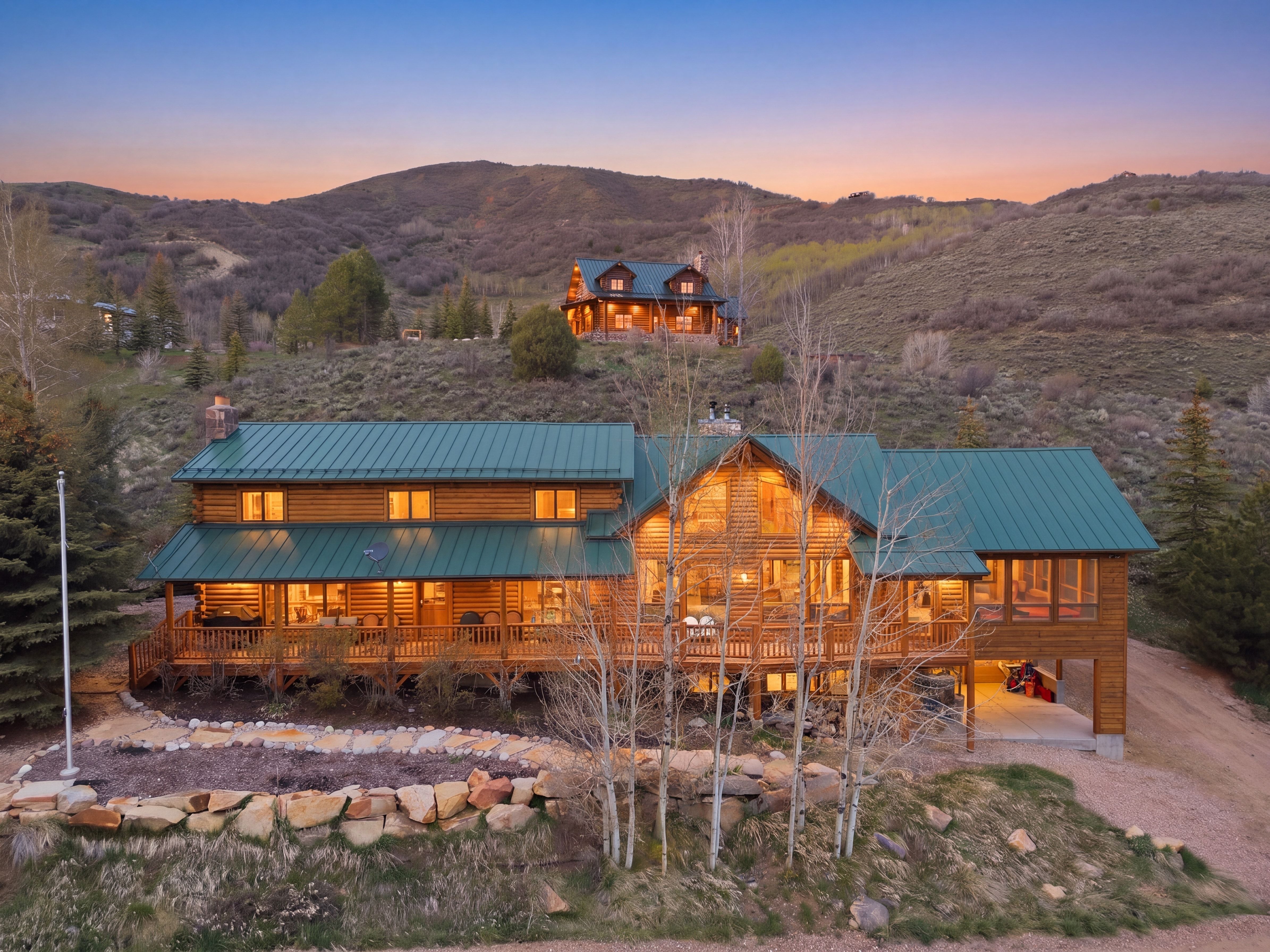 Log cabin exterior with a green metal roof, multiple windows, and an extensive wraparound porch