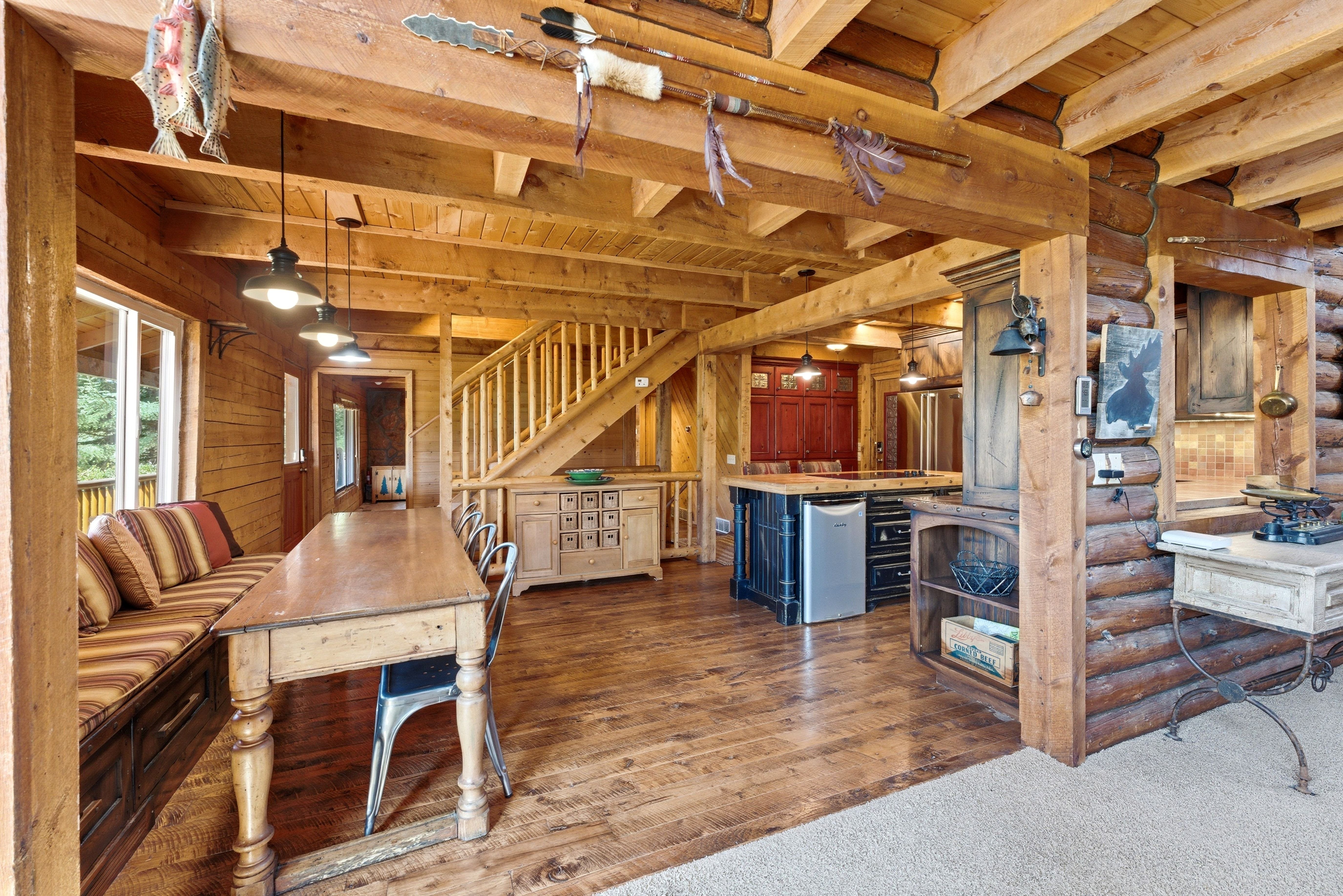 Open-concept living area featuring a log cabin aesthetic, exposed wood beams, wood-finish flooring, a built-in window seat, and a staircase with wood railings