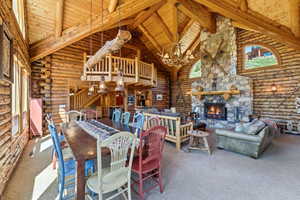 Spacious great room featuring exposed log walls, a vaulted wood-plank ceiling with exposed beams, and a substantial stone fireplace