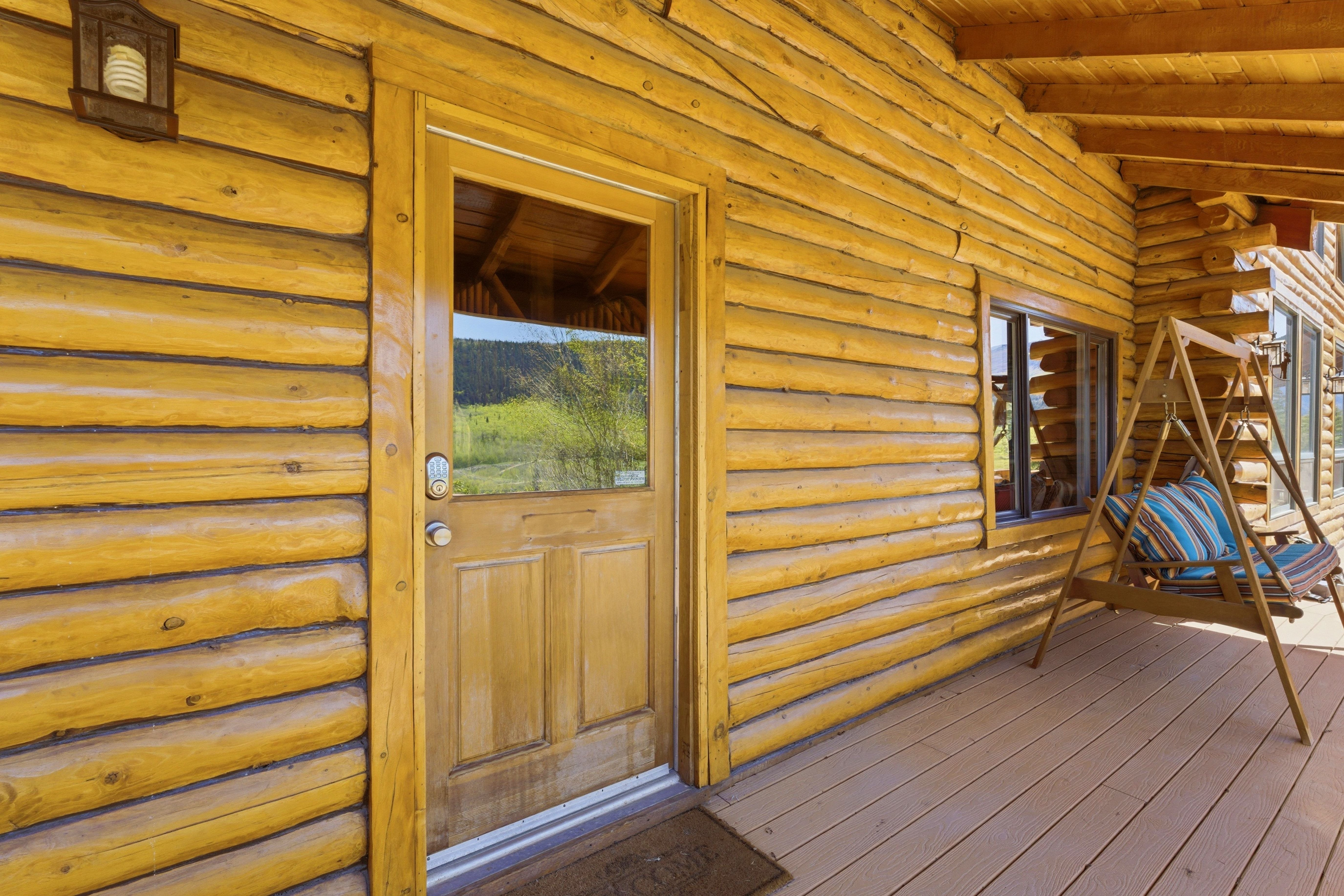 Rustic log cabin exterior with a natural wood-finish door featuring a glass upper panel and a smart lock