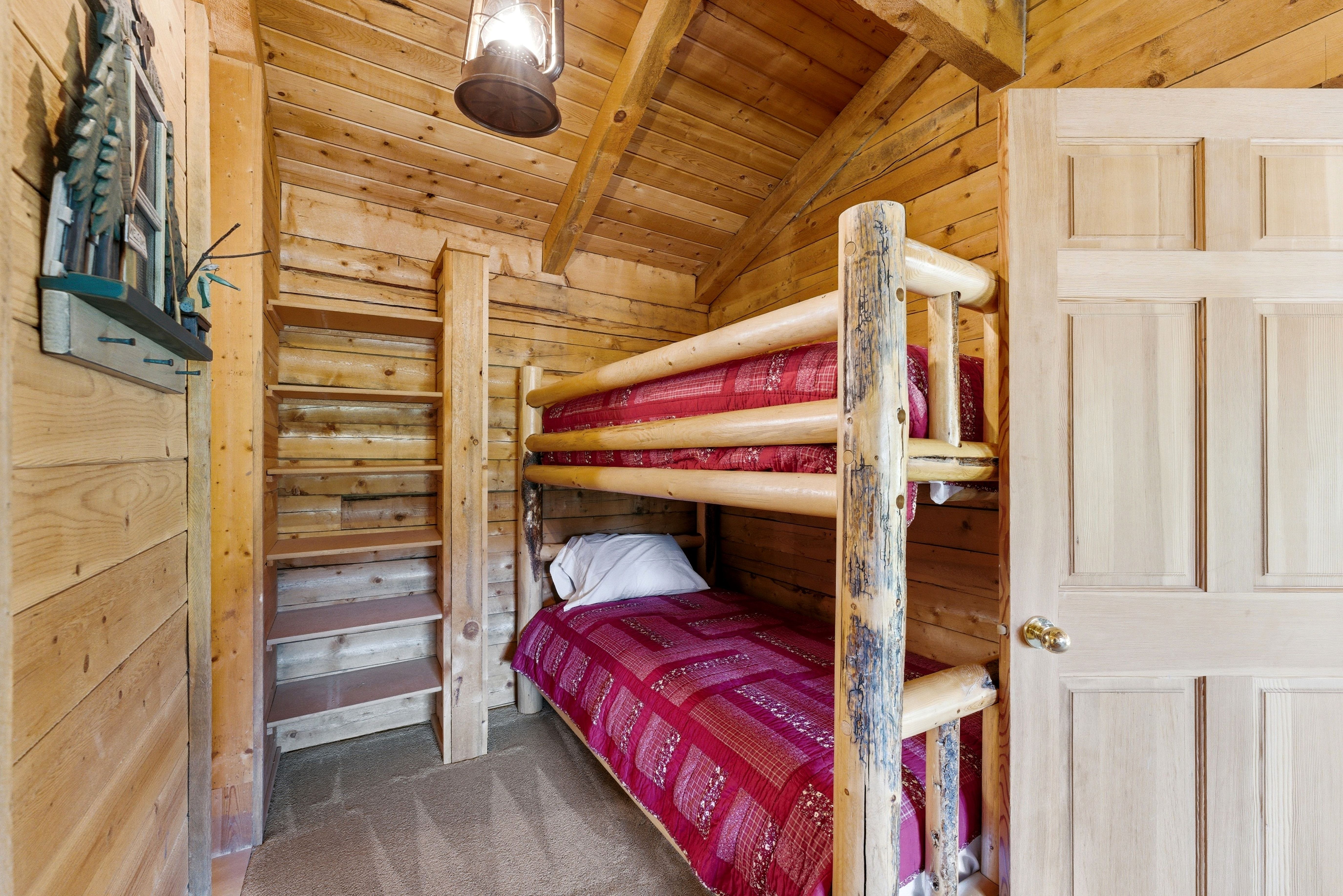 Rustic wood-paneled walls and sloped ceilings define this space, featuring built-in bunk beds with log-style frames