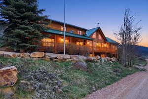 Rustic log home exterior featuring a green metal roof, multiple windows, a wraparound deck, and a stone retaining wall
