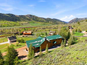 Log cabin style home with green metal roofing, set against a backdrop of mountainous terrain and a verdant valley