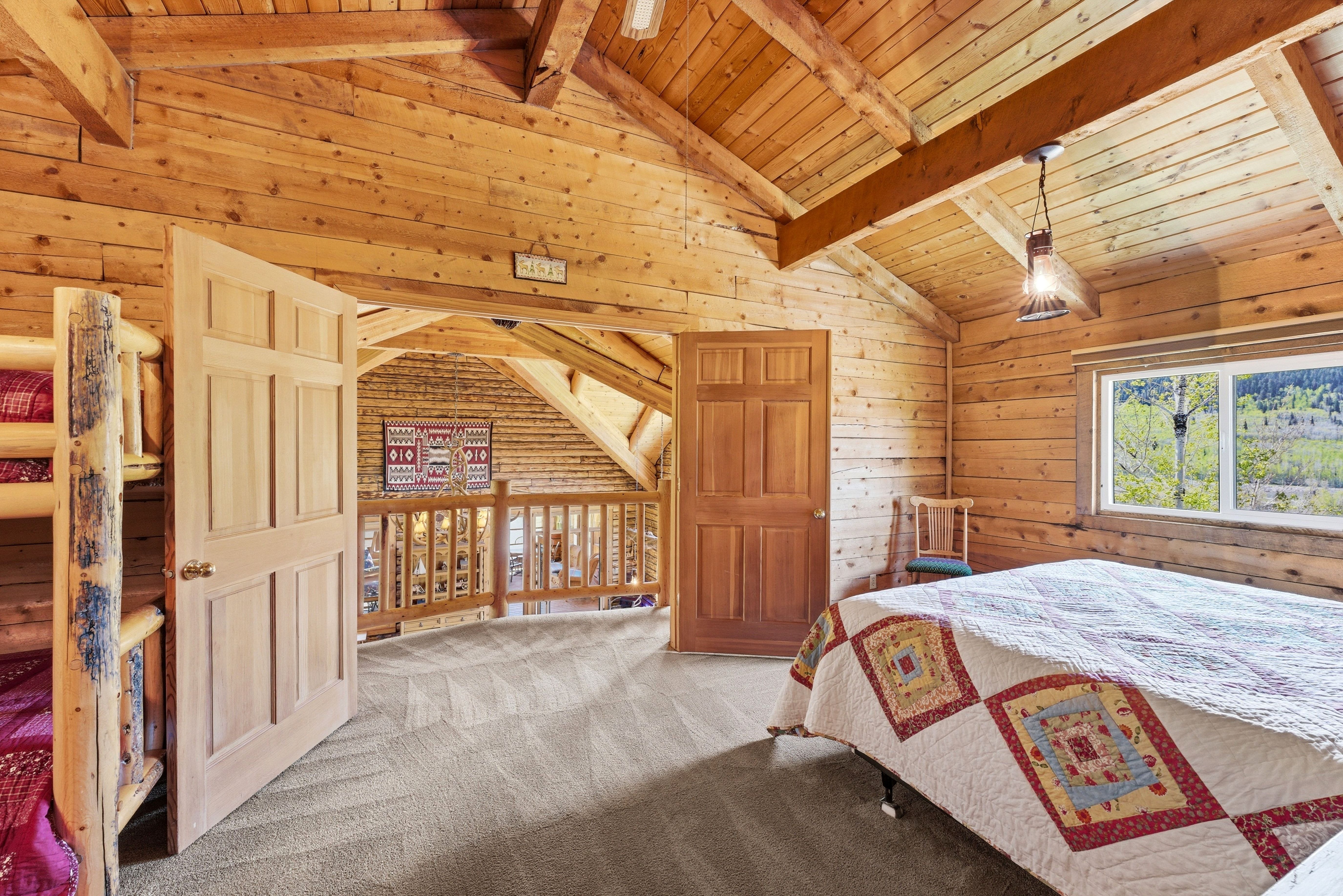 Wood-paneled room featuring vaulted ceilings with exposed beams and a window overlooking a natural landscape