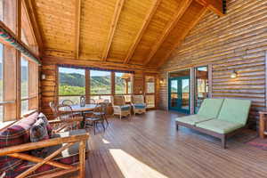 Expansive covered porch featuring wood-finish flooring, log wall construction, and a vaulted wood-plank ceiling