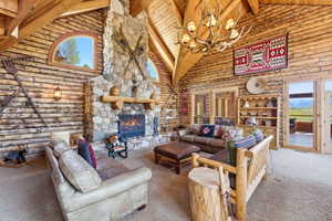 Spacious living area featuring log walls, a vaulted ceiling, and a prominent stone fireplace with a wood-beam mantel