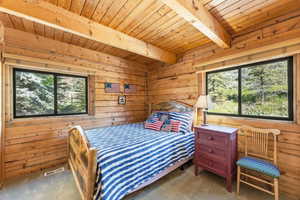 Wood-paneled room featuring exposed ceiling beams and two large windows with natural outdoor scenery