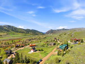 Expansive mountain valley landscape featuring multiple residential structures surrounded by lush greenery and distant peaks