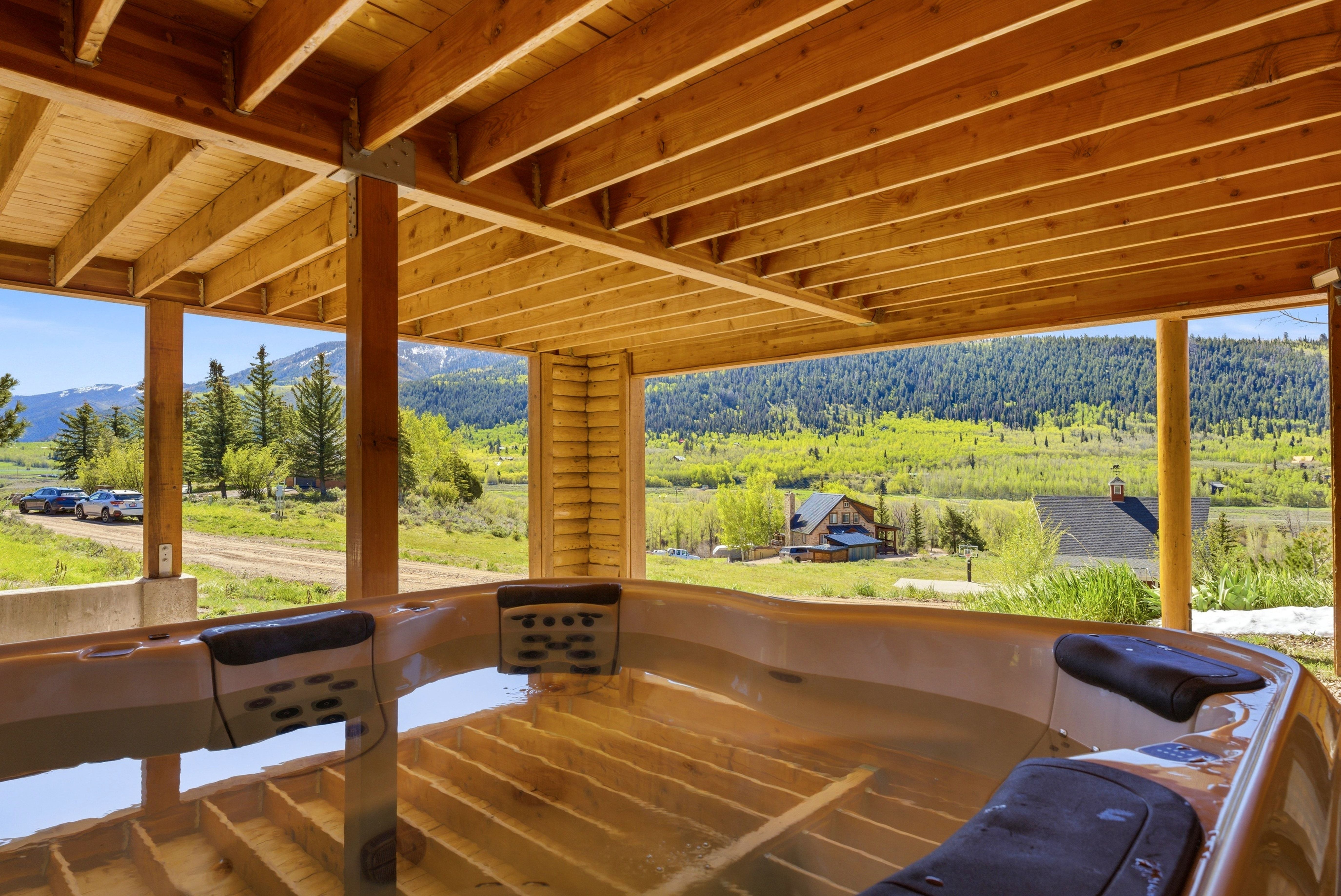 Covered outdoor spa with multiple seating positions, positioned under a wood-beamed ceiling