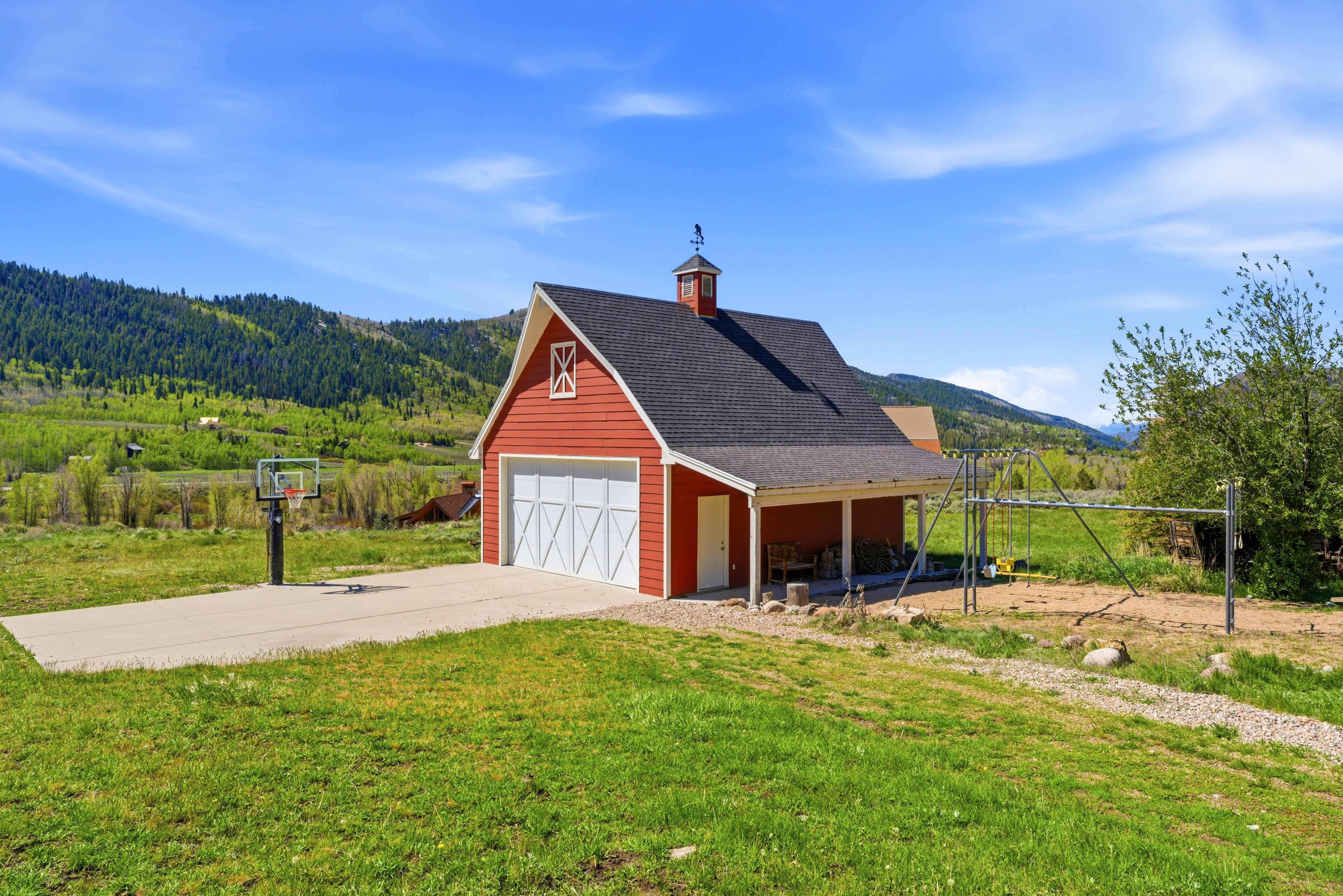 Red barn-style structure featuring a cupola, attached covered porch, white garage door, and decorative gable vent