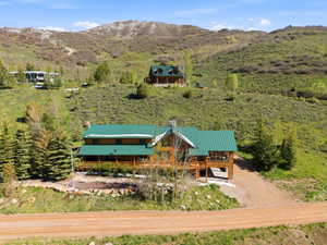 Mountain-side log home featuring a verdant metal roof, extensive decking, and an integrated carport
