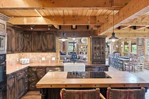Open-concept kitchen featuring wood-finish cabinetry, stainless steel appliances, a farmhouse sink, and a large central island with a built-in cooktop