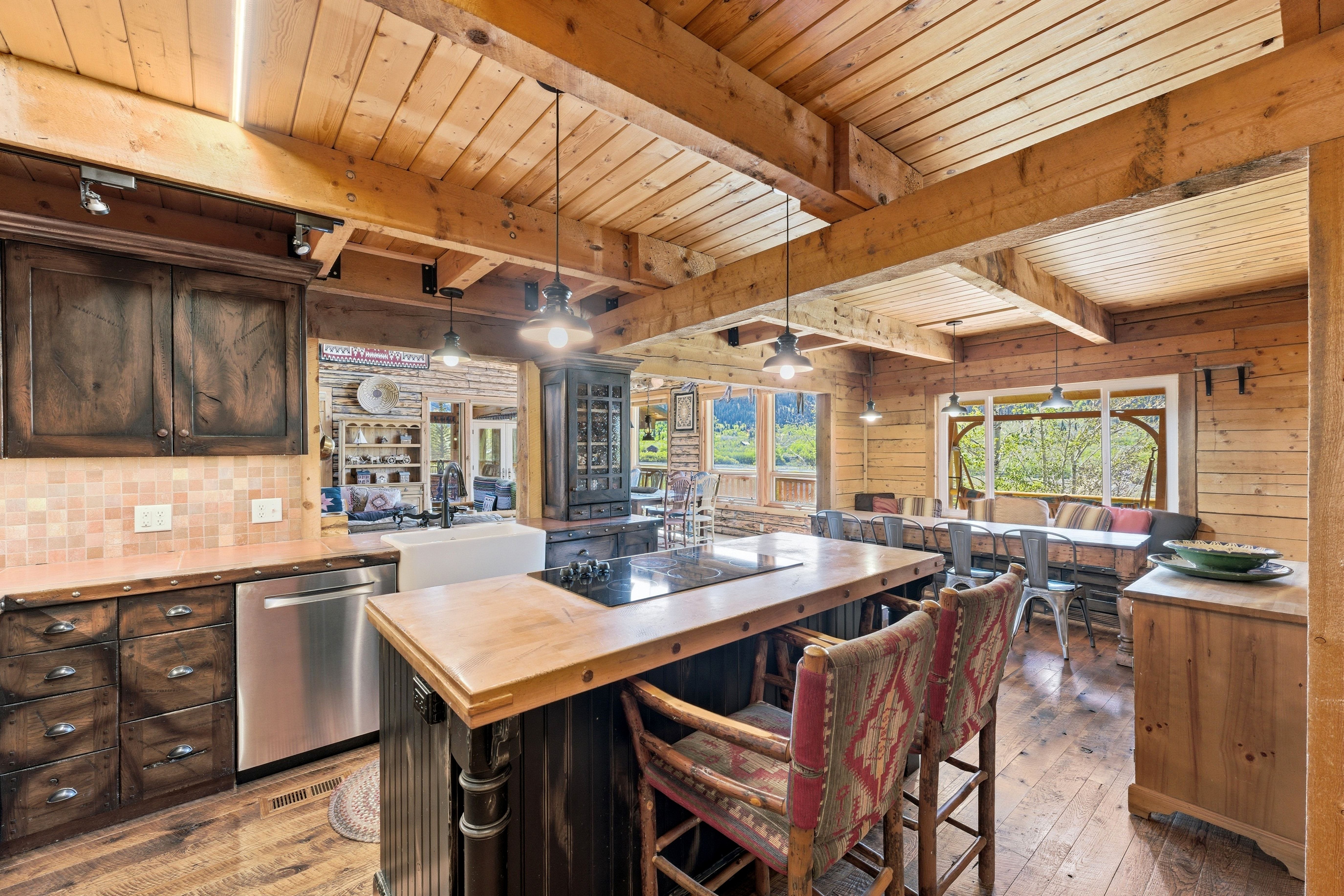 Spacious kitchen featuring exposed wood beams, a large center island with a cooktop, a farmhouse sink, stainless steel appliances, and wood-finish flooring
