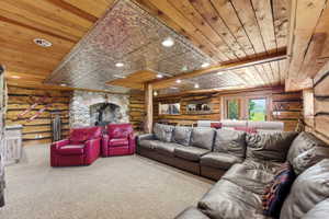 Spacious living area featuring log walls, wood plank ceiling, stone fireplace with insert, recessed lighting, and double glass doors
