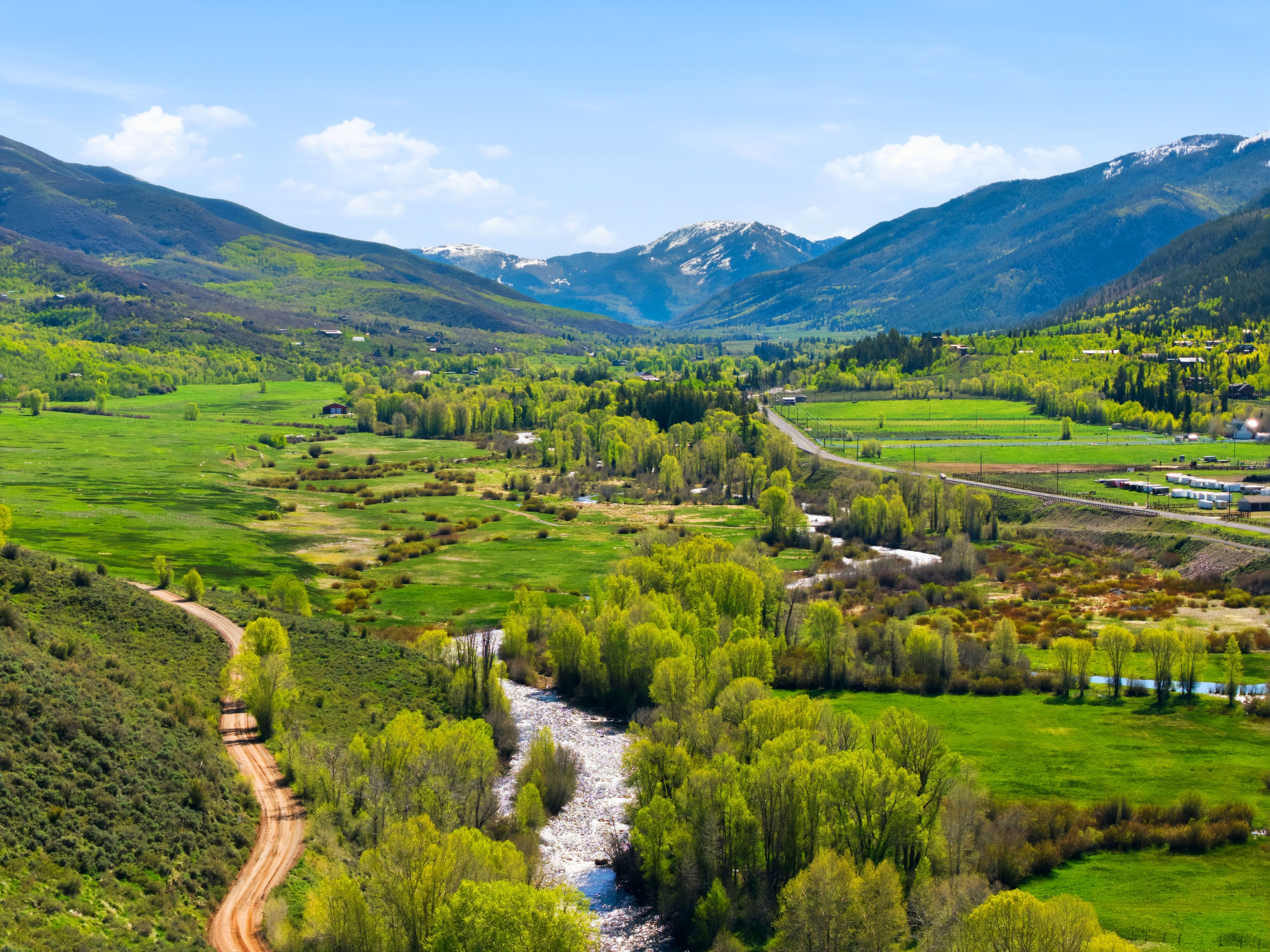 Expansive valley setting featuring a winding river, verdant fields, and mature deciduous trees