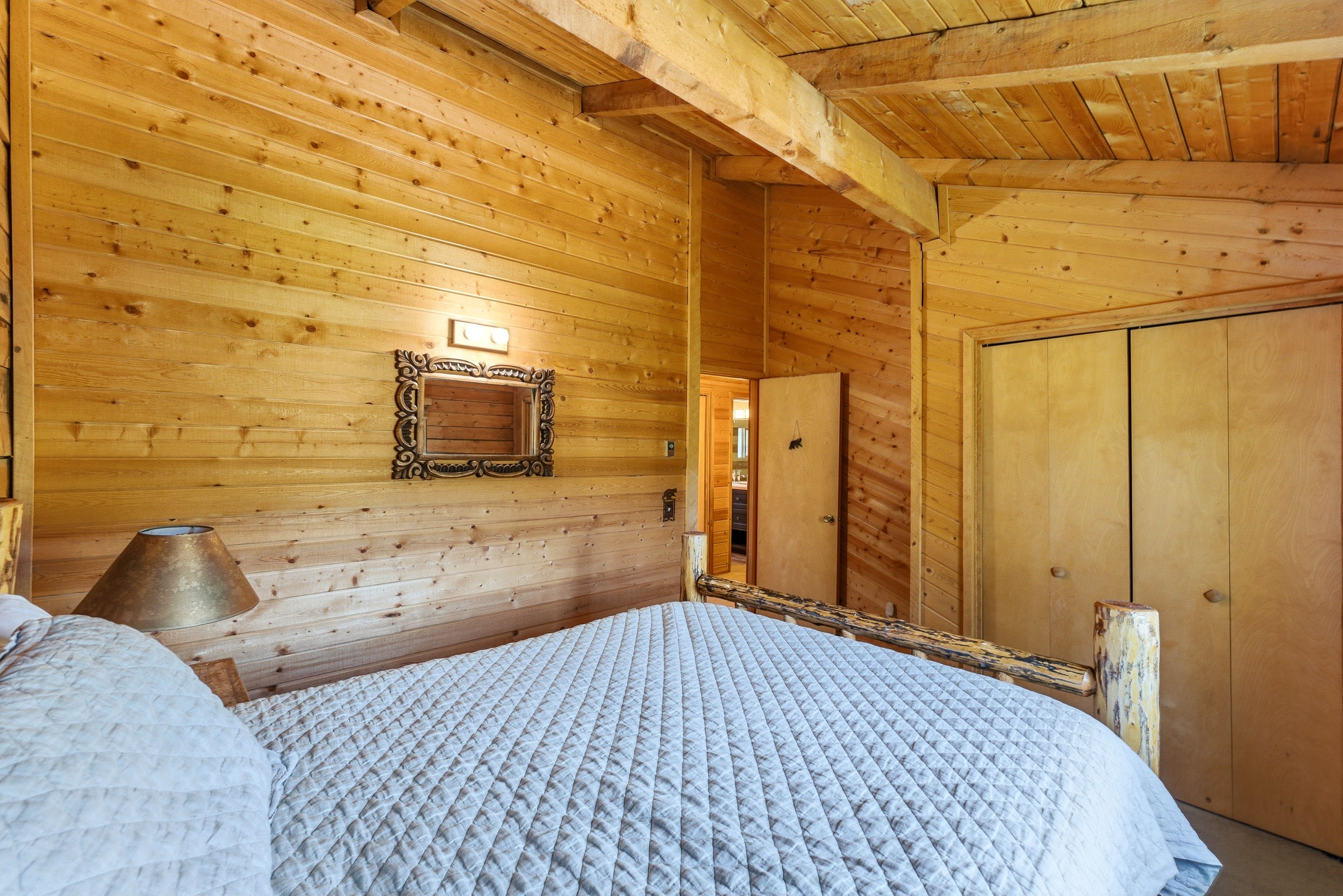 Pine plank walls and ceiling, exposed wooden beams, natural wood bed frame, wood bi-fold closet doors, and recessed wall niche with decorative trim