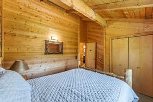 Pine plank walls and ceiling, exposed wooden beams, natural wood bed frame, wood bi-fold closet doors, and recessed wall niche with decorative trim