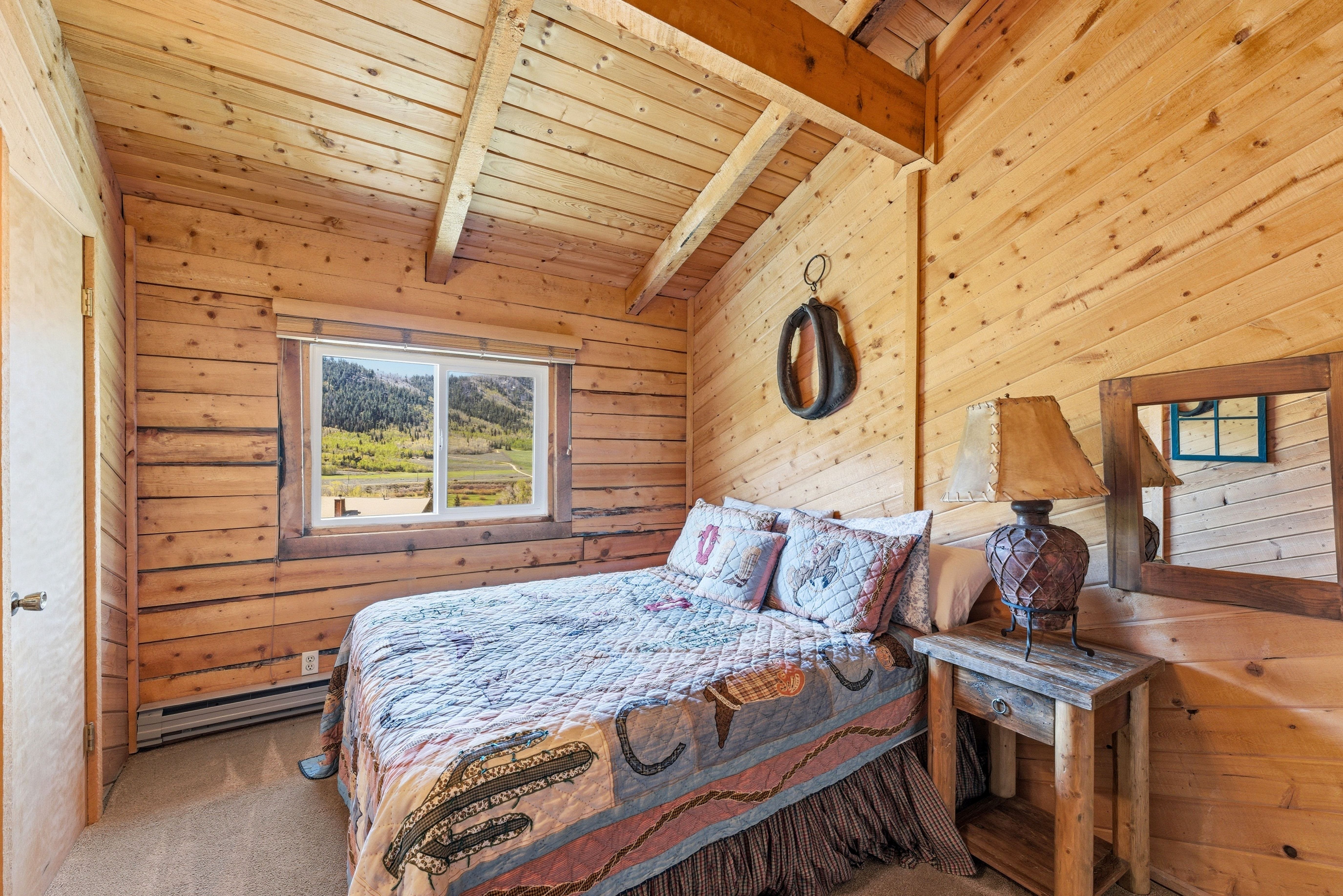 Wood-paneled room featuring a window with mountain scenery, exposed ceiling beams, and light-toned carpet flooring