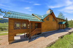 Log cabin exterior featuring a green metal roof, a screened porch, a stone chimney, a covered entryway, and a gravel driveway