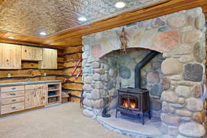 Stone fireplace with a cast iron stove, wood-paneled walls, a pressed tin ceiling, recessed lighting, and built-in wood cabinetry with a sink