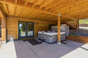Covered patio featuring a hot tub, log siding, and exposed wood beam ceiling