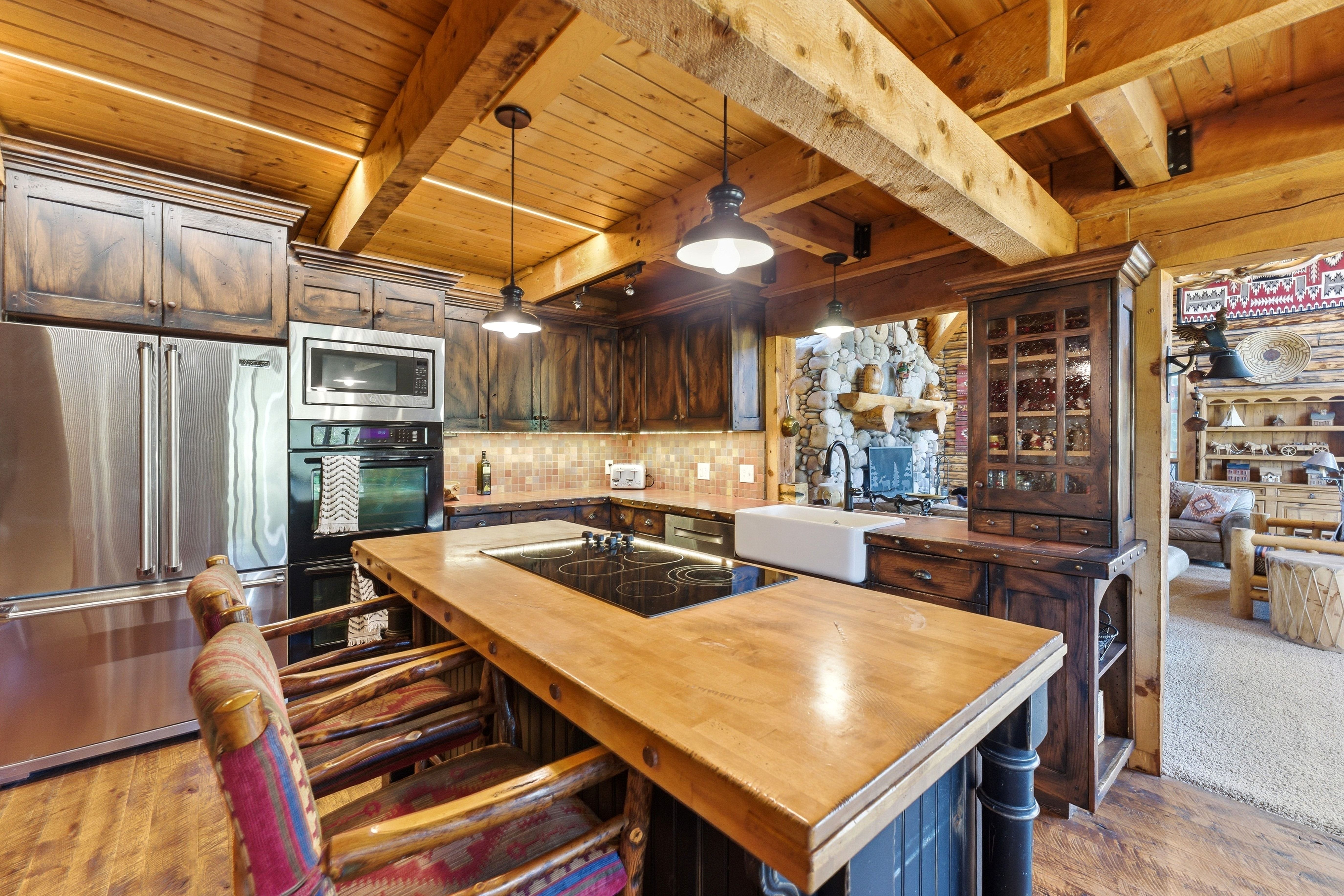 Kitchen featuring extensive wood cabinetry, stainless steel appliances, a center island with a cooktop, a farmhouse-style sink, and exposed wood ceiling beams