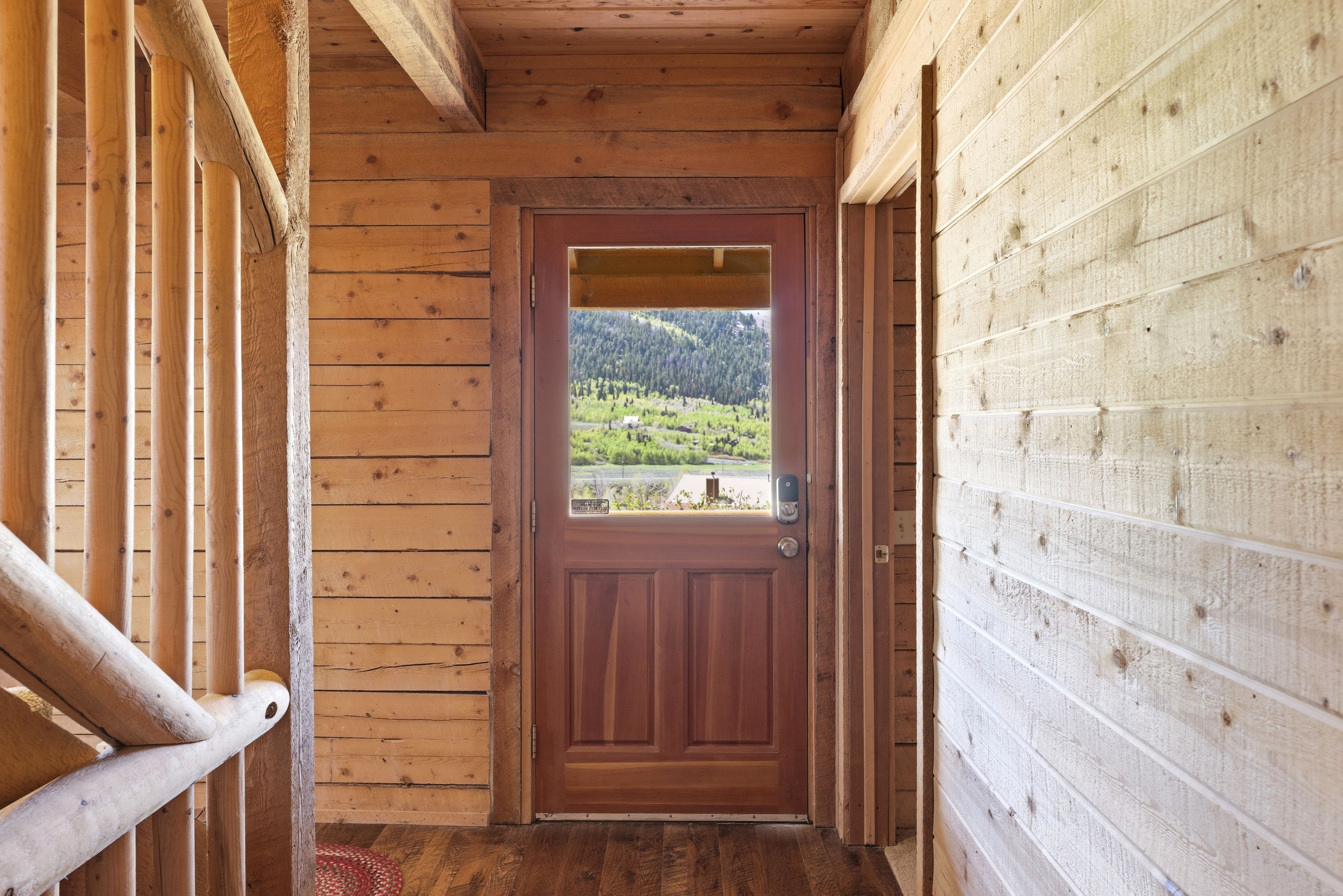 Wood-paneled interior featuring a solid wood door with an upper window, log-style banister, and wood-finish flooring