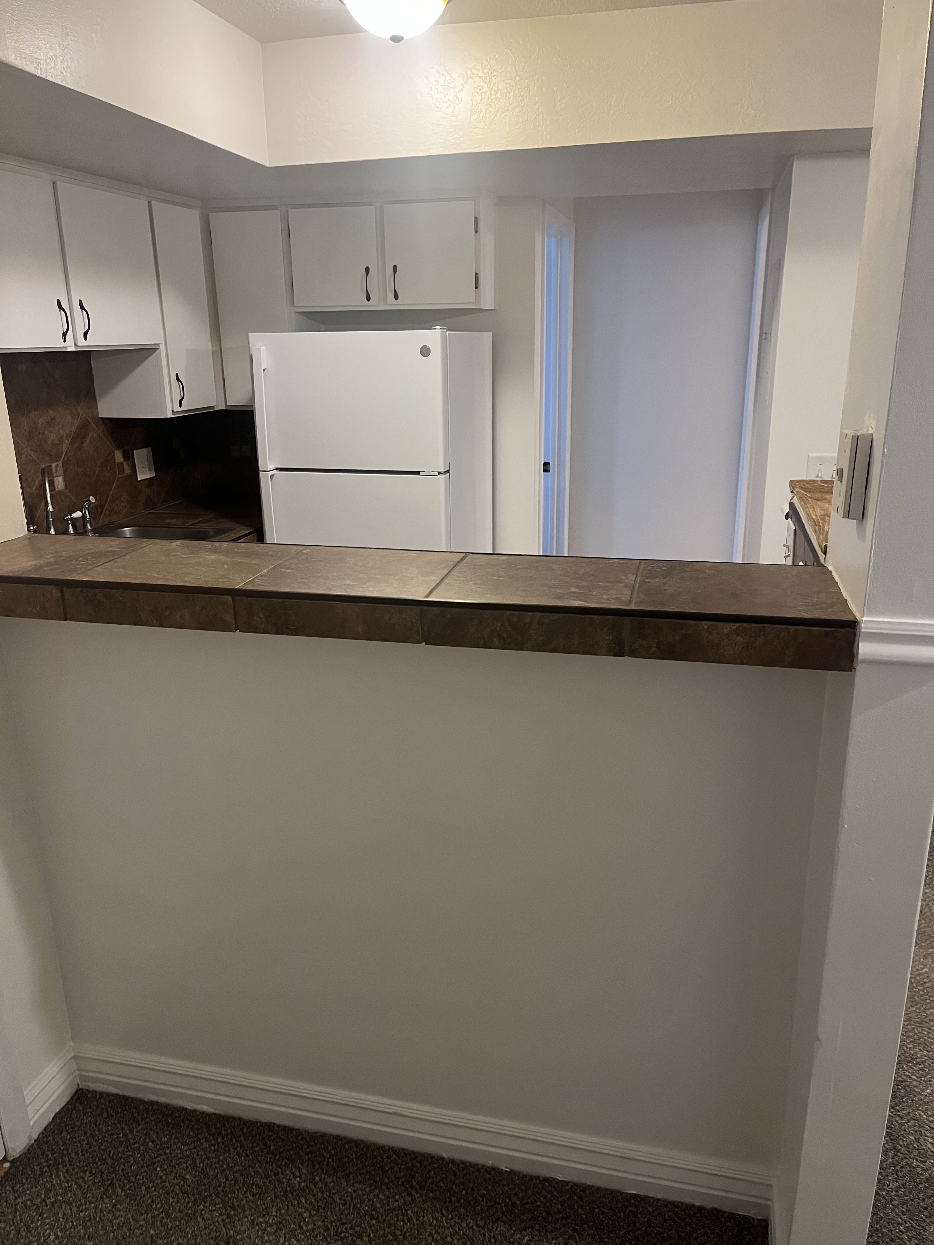 Kitchen featuring white cabinetry, a built-in sink, a refrigerator, and a tiled breakfast bar