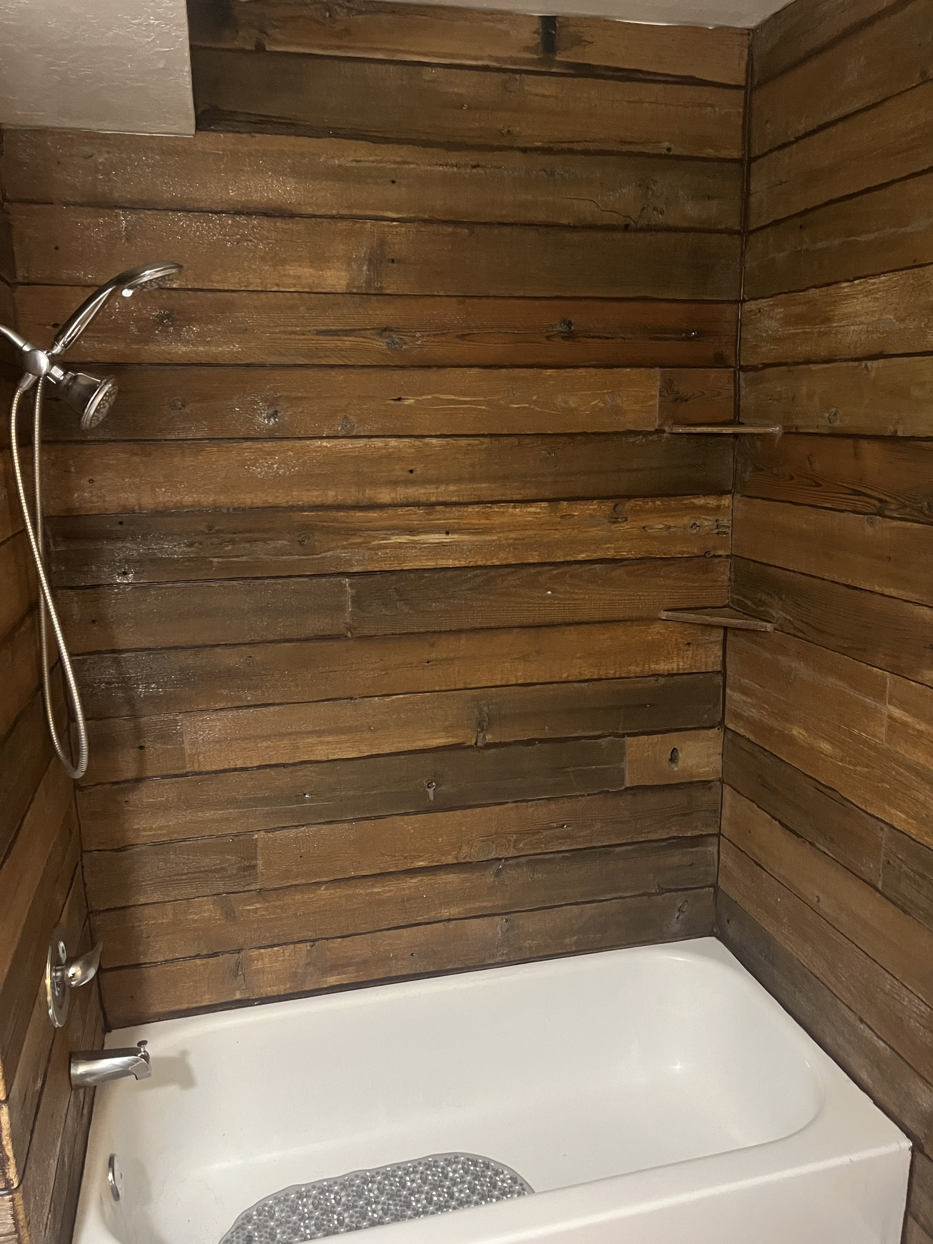 Bathtub and shower combination featuring wood-finish wall paneling, a chrome showerhead with a flexible hose, and coordinating chrome fixtures